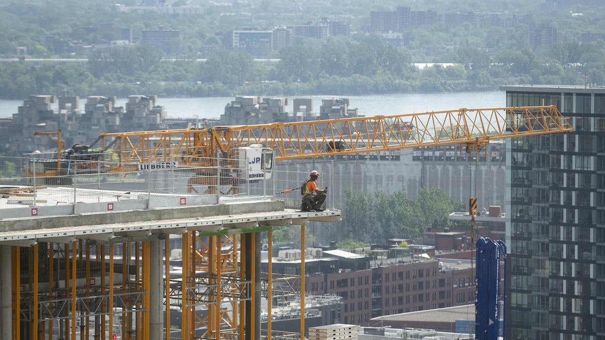 Un ouvrier de la construction travaille sur un immeuble en hauteur et on aperçoit une grue à l'arrière.