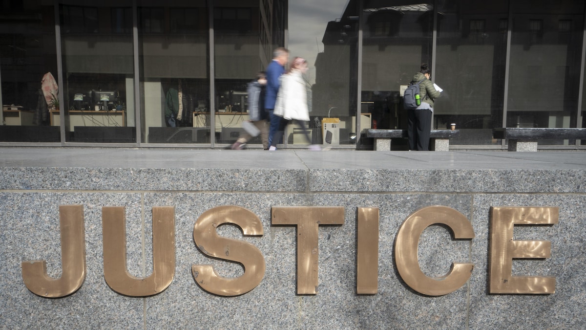Un couple avec un enfant marche et une femme portant un sac à dos regarde une feuille devant le palais de justice de Montréal, avec à l'avant-plan le logo «Justice».