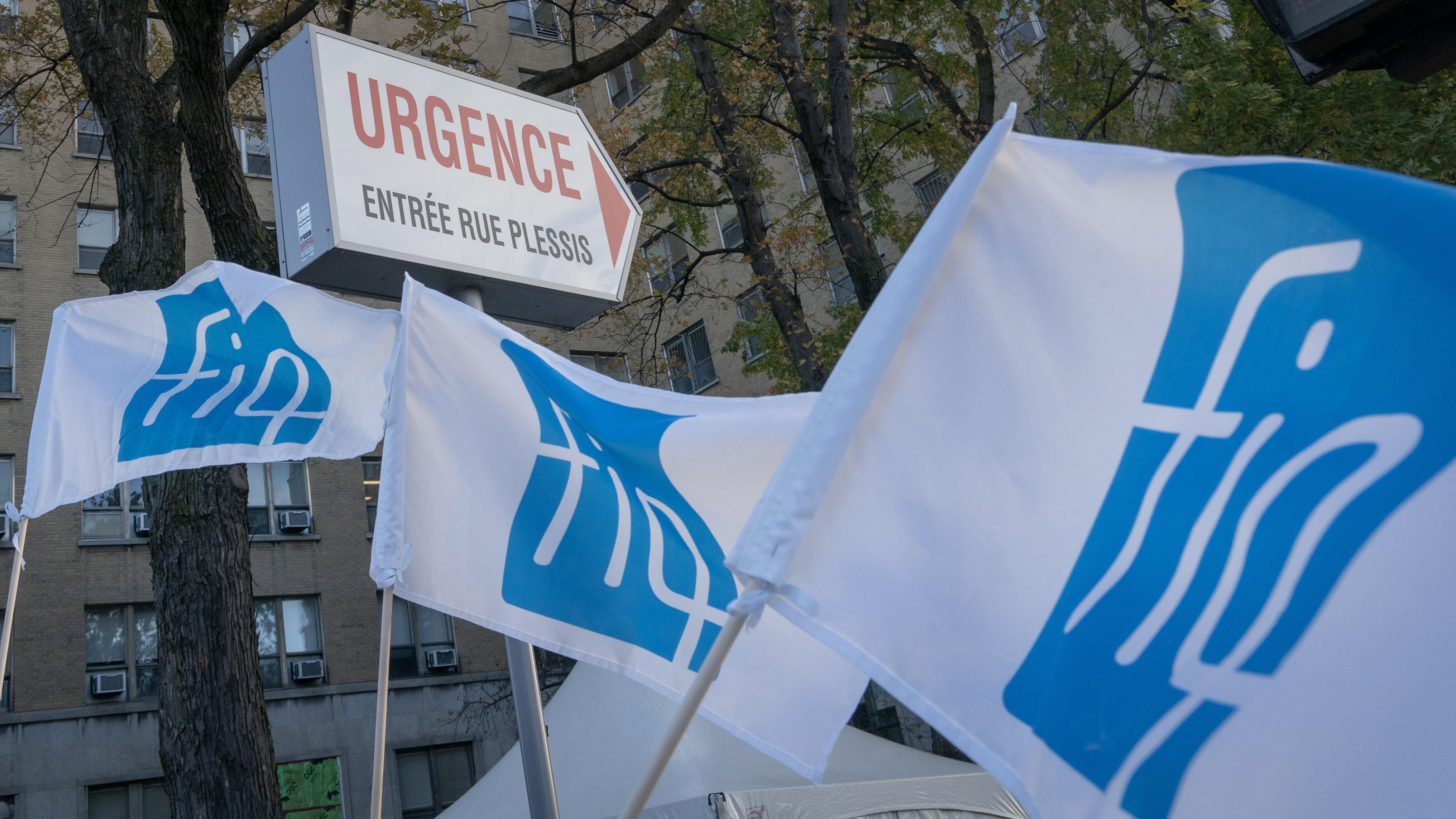 Trois banderoles de la FIQ, dans le vent, devant les urgences d'un hôpital.