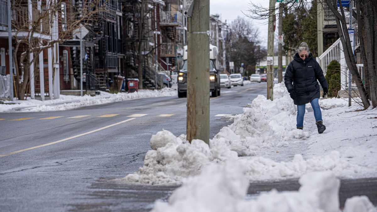 Une femme enjambe la neige poussée sur un trottoir.