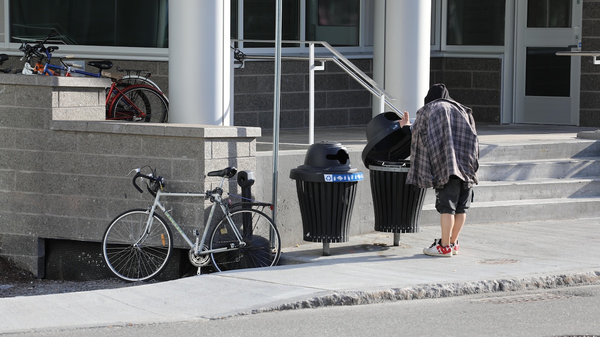 Une personne fouille dans une poubelle devant un refuge pour personnes sans-abris.
