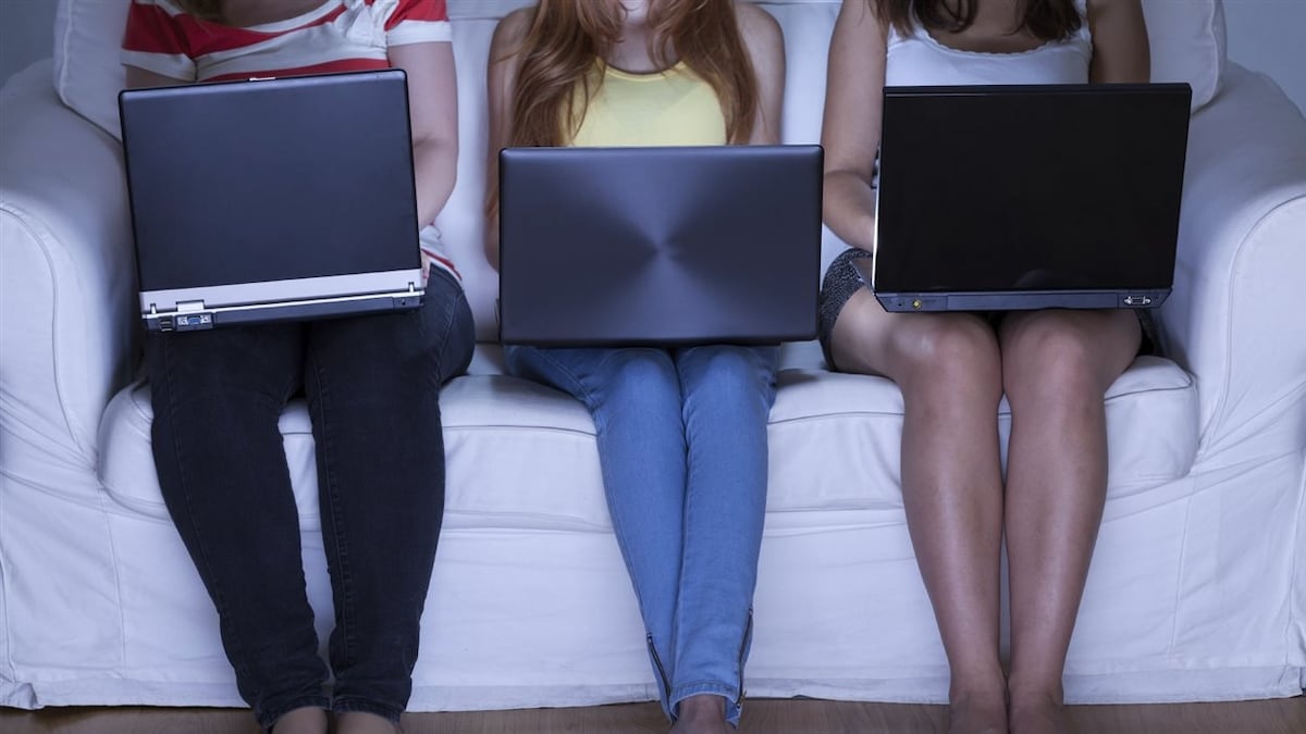 Trois personnes, côte à côte sur un divan, regarde leur ordinateur.