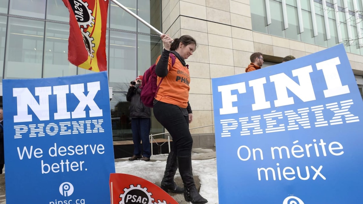 Manifestants et pancartes dénonçant à l'extérieur d'un édifice pour dénoncer les conséquences des ratés du système de paie Phénix. 