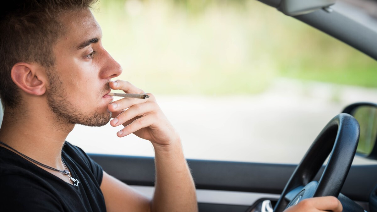 Un jeune homme conduit une voiture en fumant son joint de cannabis. 