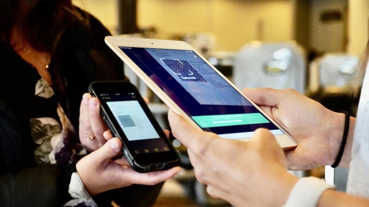 Une employée tient une tablette électronique pour scanner un code QR sur le téléphone d'une cliente.