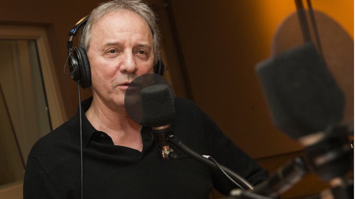 Le comédien Michel Côté portant un casque d'écoute devant un micro de Radio-Canada. 