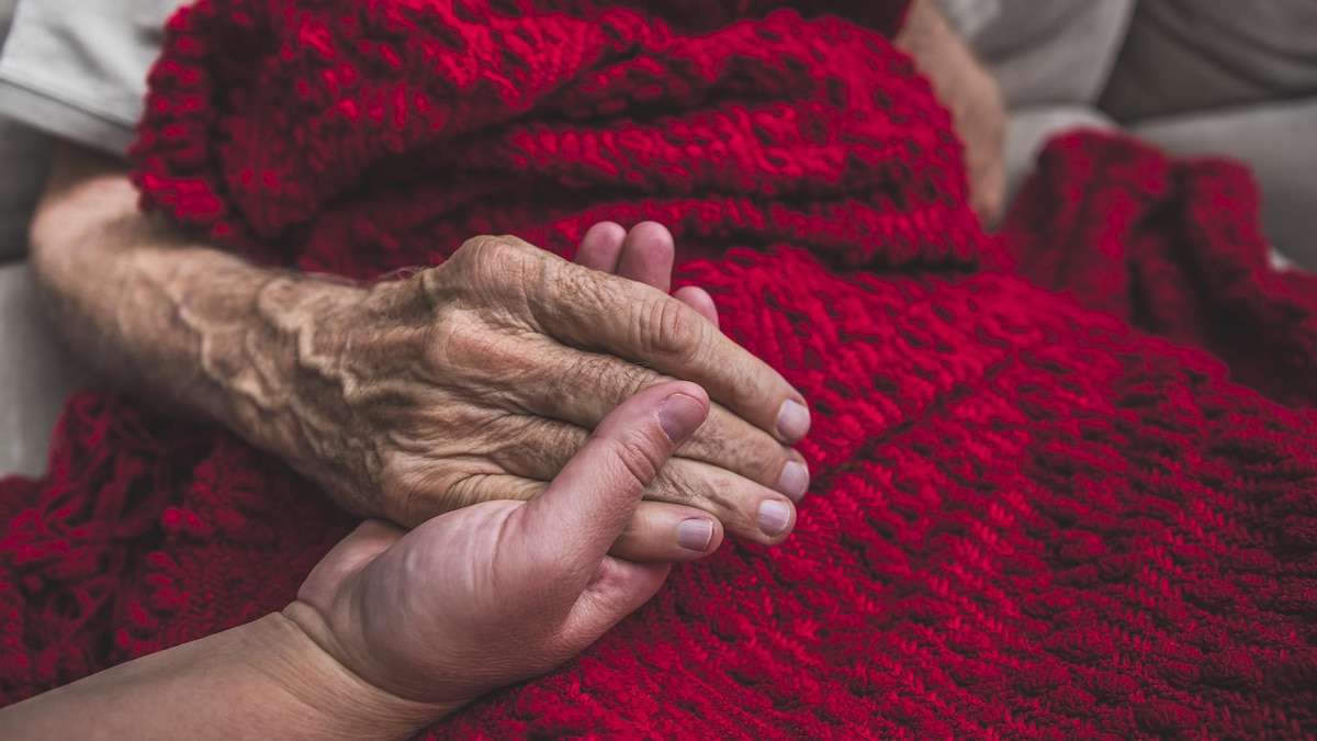 Gros plan sur la main d'une personne âgée dans la main d'une autre personne.