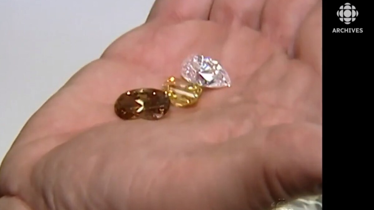 Trois diamants: un incolore, un jaune et un de couleur ambrée se trouvent dans le creux d'une main.