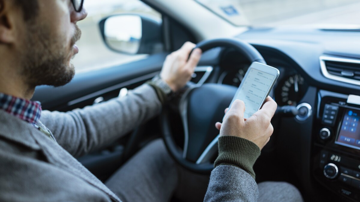 Un homme utilise son cellulaire au volant de sa voiture.