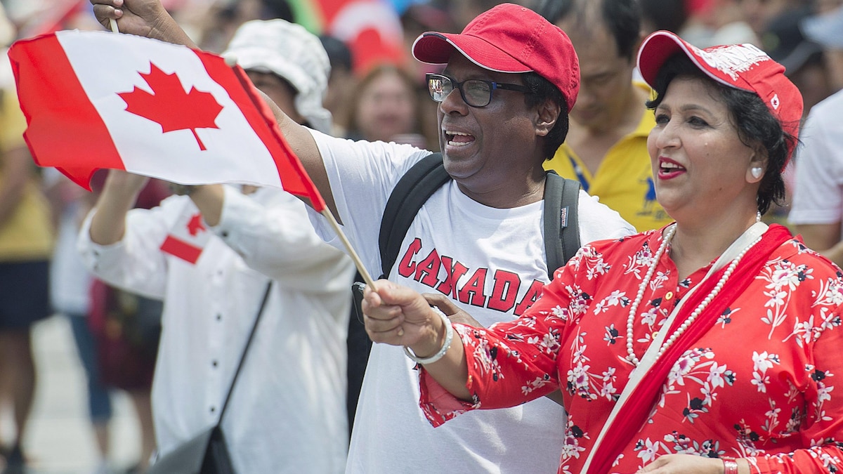 Deux personnes habillées de rouge et blanc agitent des drapeaux canadiens lors d'une parade de la fête du Canada à Montréal. 