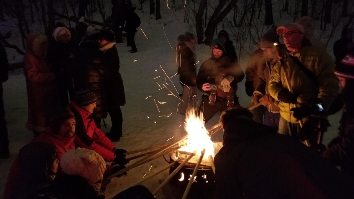 Des gens, la nuit, dans une forêt autour d'un feu de camp, tenant des bâtons dans leurs mains.