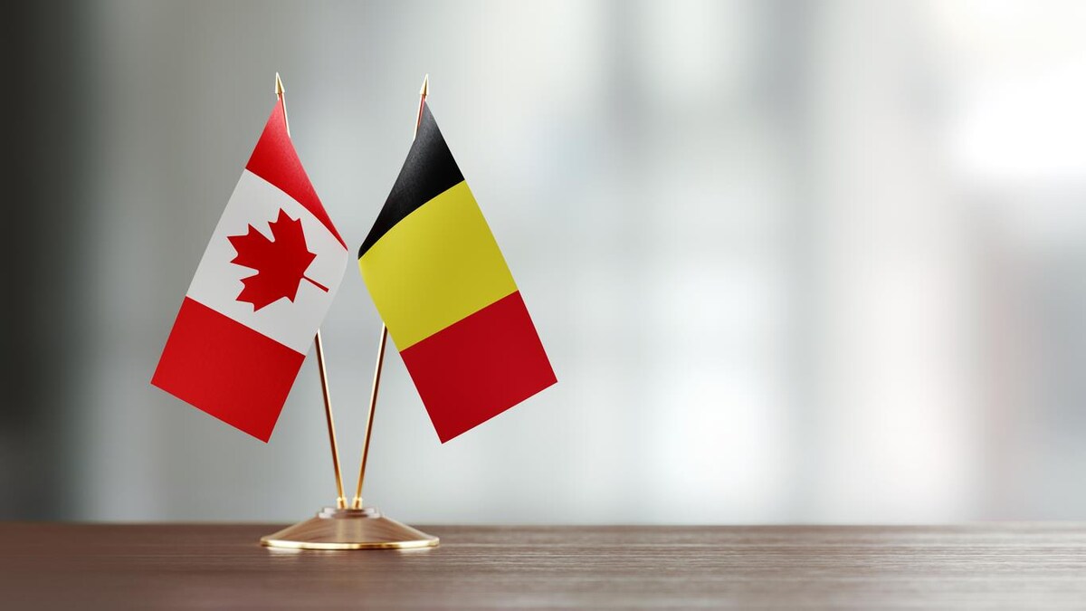 Un drapeau canadien et un drapeau belge sur un socle, sur une table.