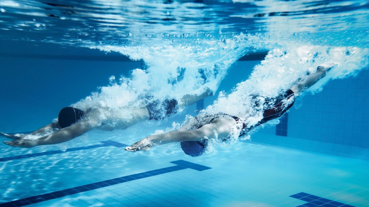 Deux nageurs font un départ sous l'eau les mains devant.