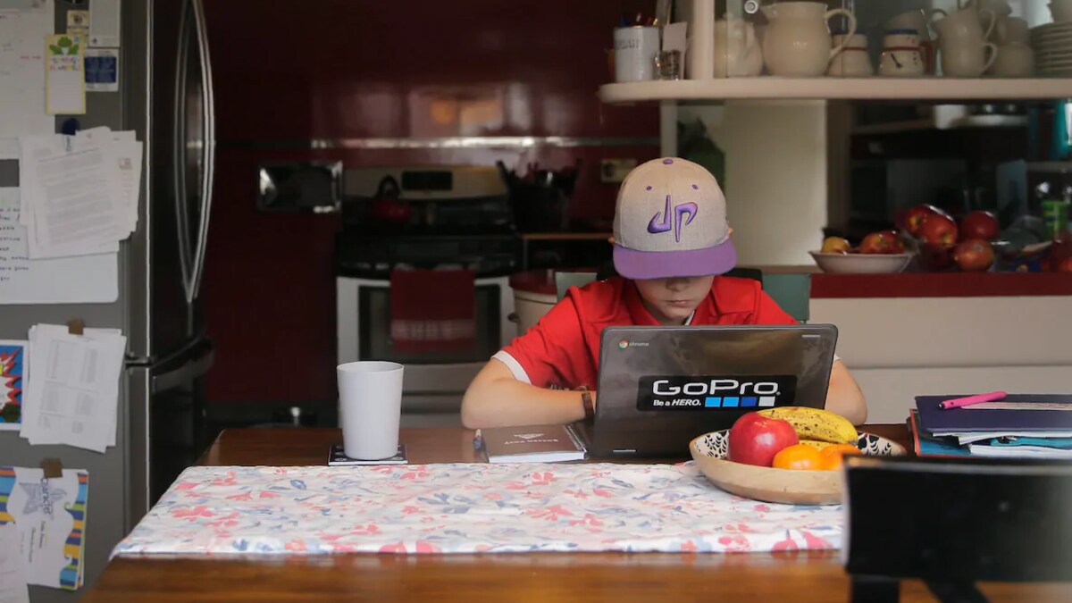Un garçon utilise un ordinateur portable sur une table de cuisine.