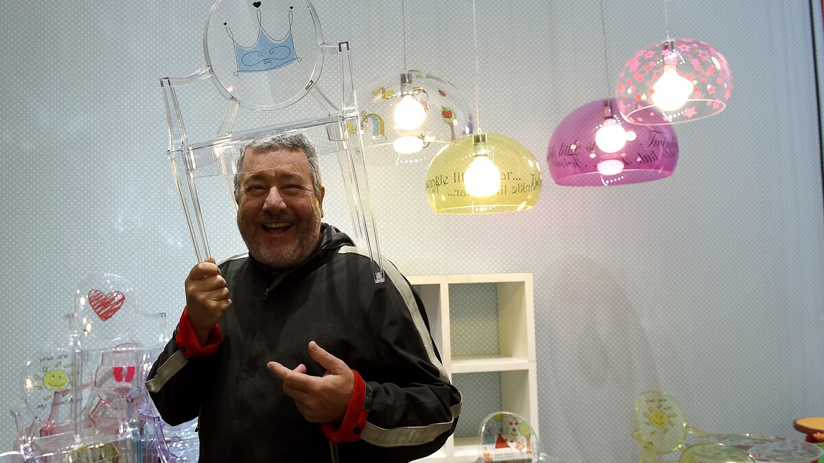 Le designer Philippe Starck prend la pose, souriant, avec une chaise transparente sur la tête.