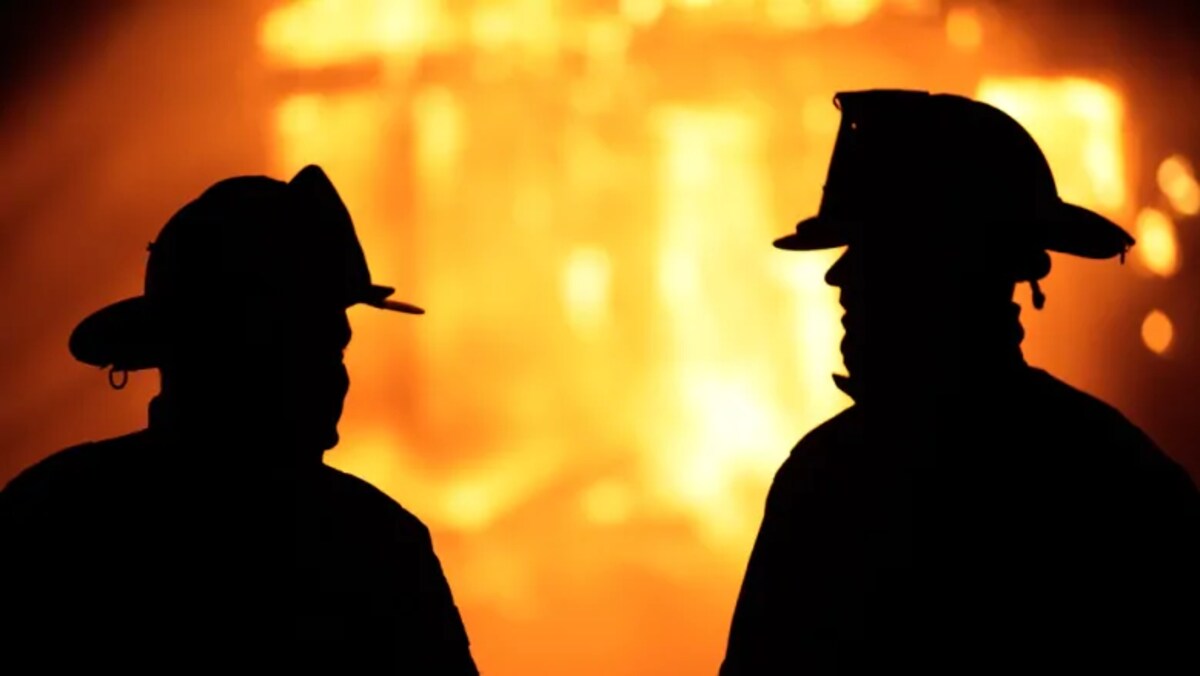 Silhouette de deux pompiers dans une lumière jaune orangée qui évoque un incendie.