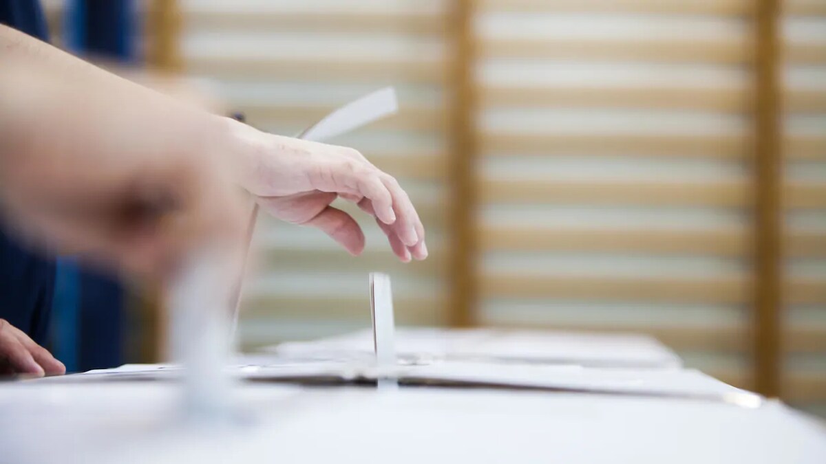 Une personne dépose un bulletin de vote dans une boite.