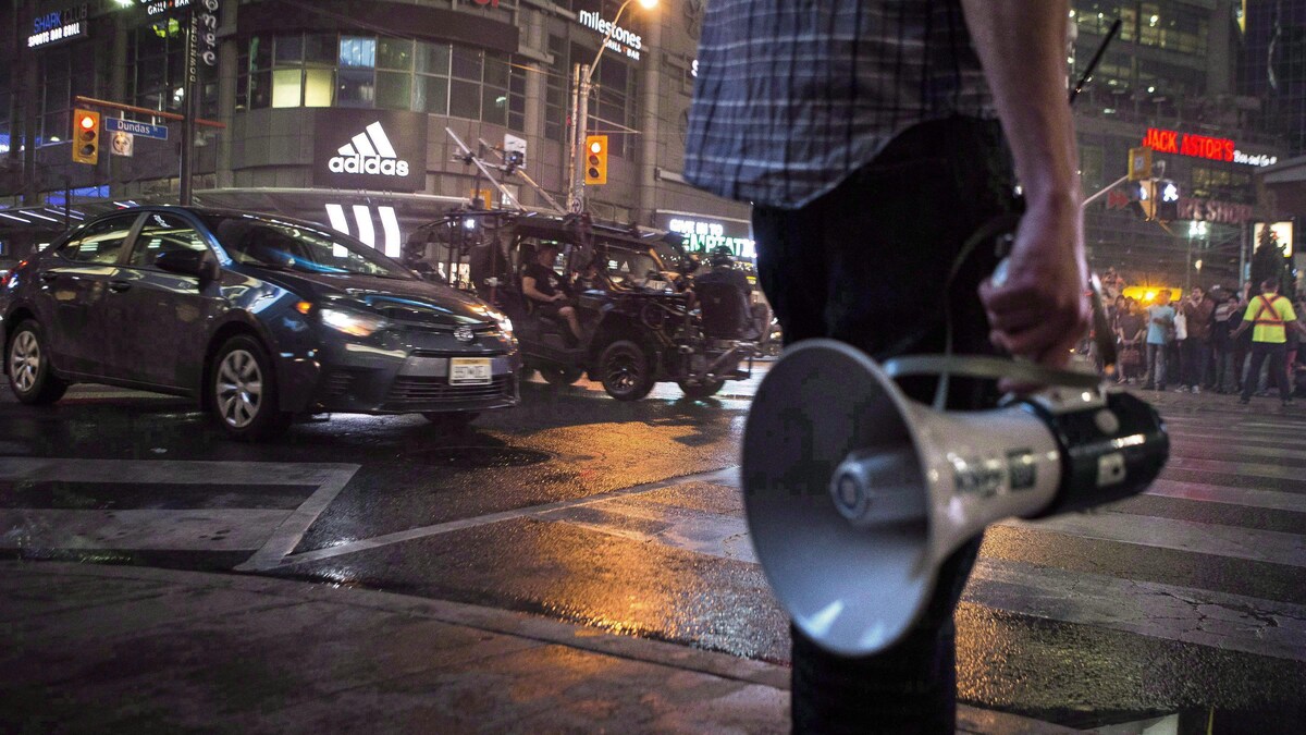 Un assistant tient un porte-voix près de la rue Yonge où est tournée une scène du film Suicide Squad avec une voiture.