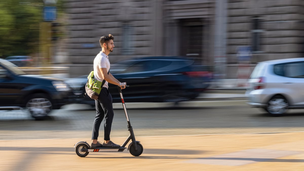 Un homme de profil sur une trottinette électrique en milieu urbain. 