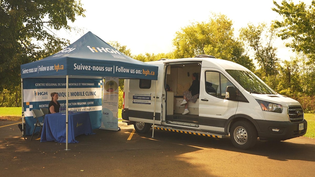 Une clinique mobile dans une fourgonnette est installée dans un stationnement près d'un parc.