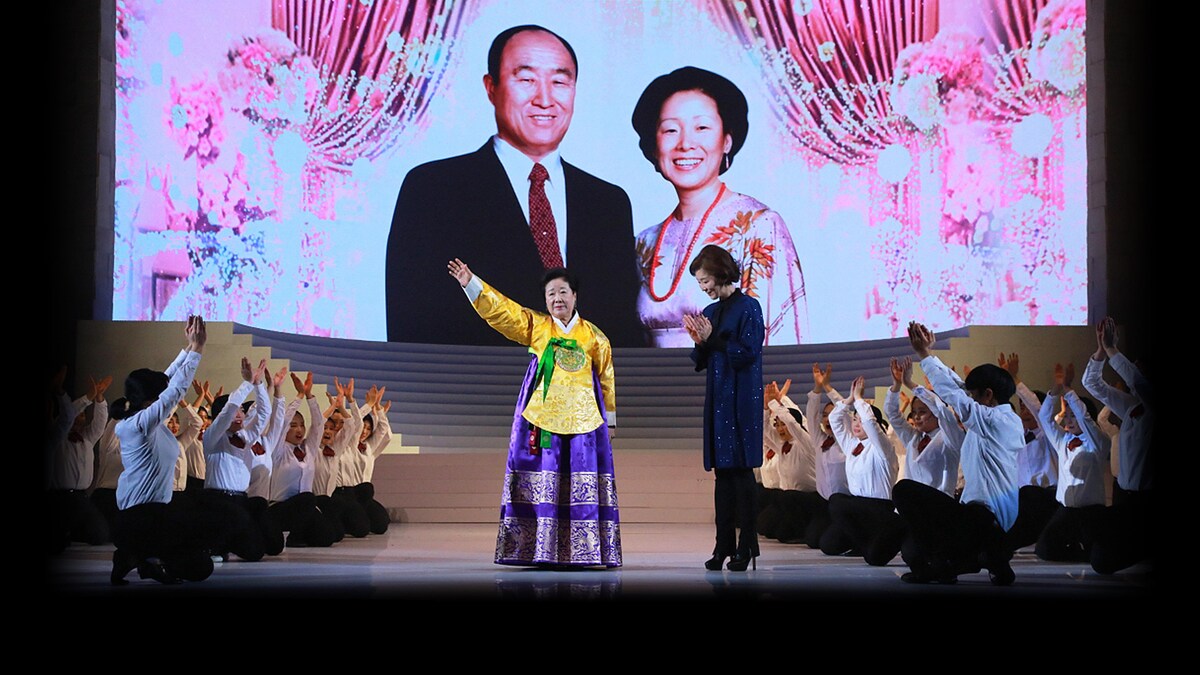 Hak Ja Han Moon sur une scène au milieu d'enfants brandissant les bras vers le ciel.