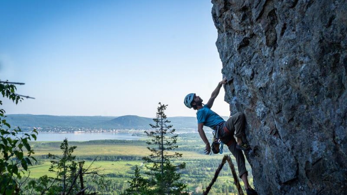 Une personne pratiquant l'escalade de roche avec une vue sur la Baie-des-Chaleurs.