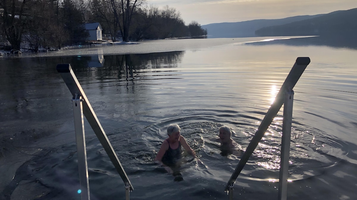 Deux personnes rient dans l'eau froide du lac en hiver. 