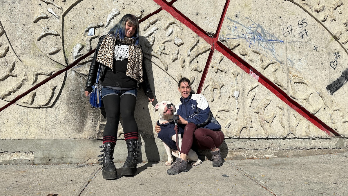 Deux femmes et un chien appuyés sur un mur de béton.