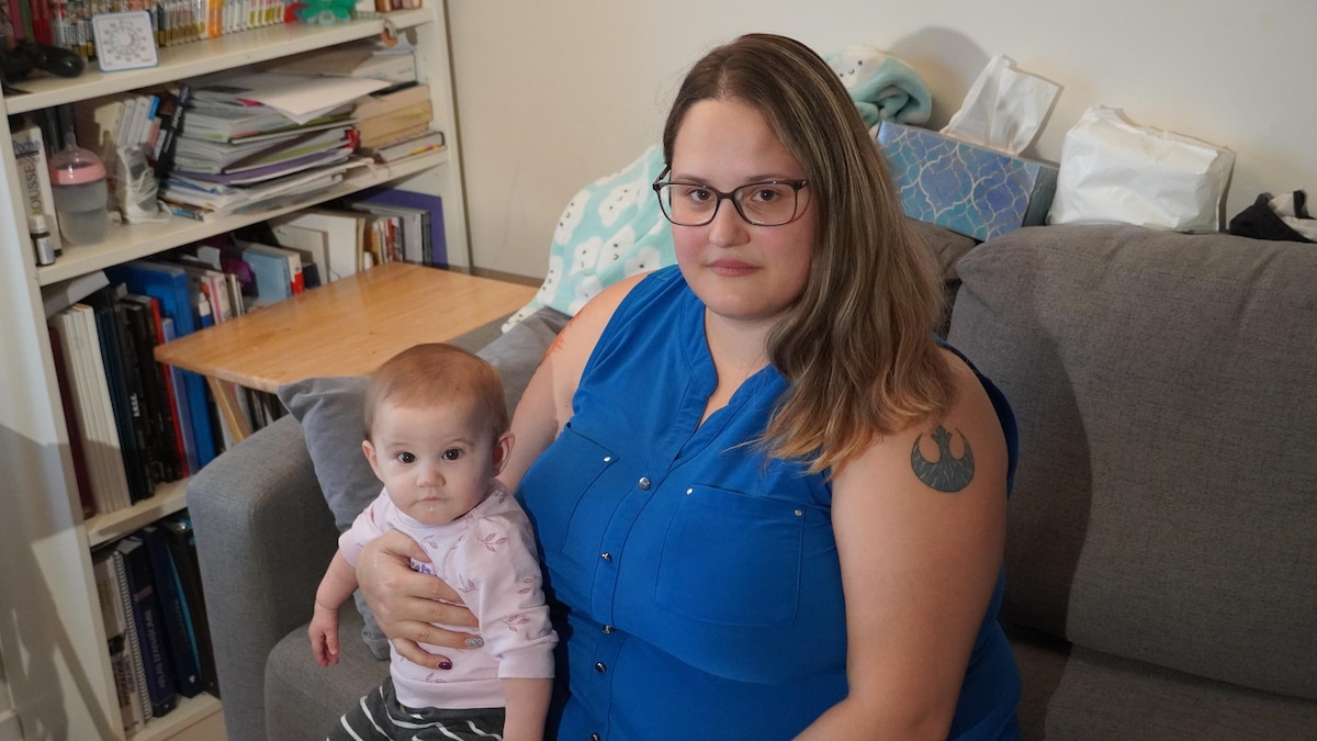 Une femme assise sur un divan tient un bébé dans ses bras.