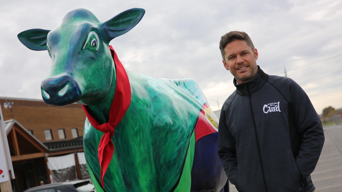 Michel-Olivier Matte aux côtés d'une sculpture de vache décorée et peinturée.
