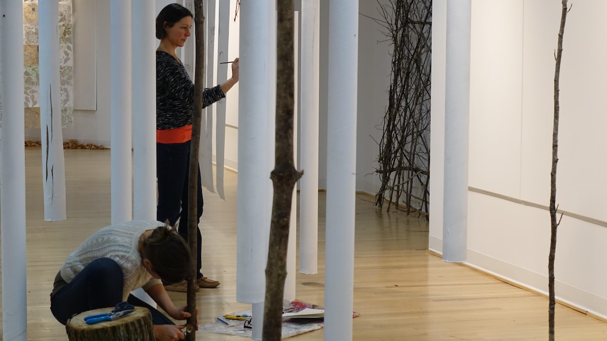 Deux femmes fignolent les dernières étapes de mise en place d'une exposition en galerie où les arbres sont mis en valeur.