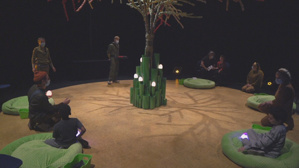 Spectateurs assis sur des coussins, en cercle autour d'un arbre décoratif.