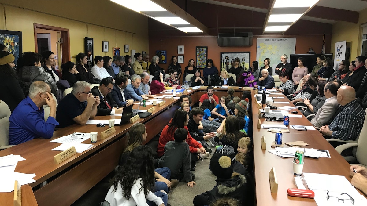 Les maires du Témiscamingue assis autour d'une table, dans une salle de réunion remplie de citoyens.
