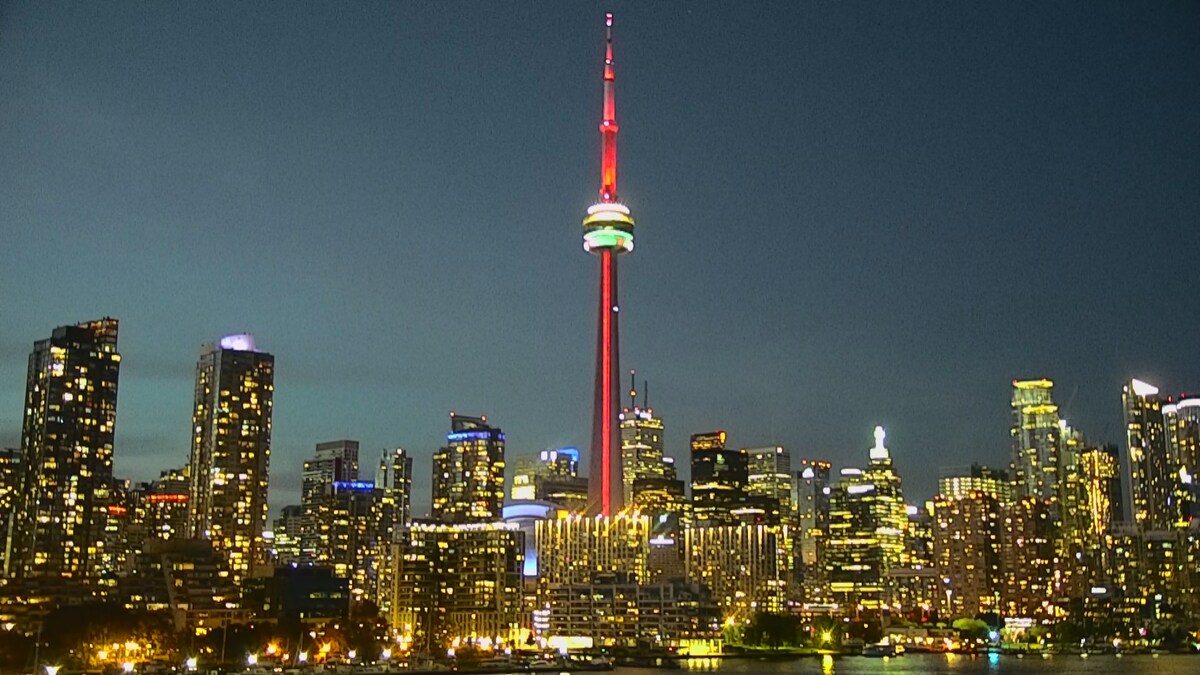 La Tour CN à Toronto illuminée de rouge, blanc et vert au milieu des tours du centre-ville.
