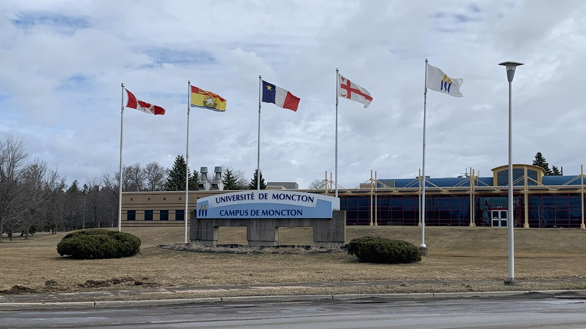 L'enseigne du campus devant les drapeaux du Canada, du Nouveau-Brunswick, de l'Acadie et du Grand Conseil mi'kmaq.