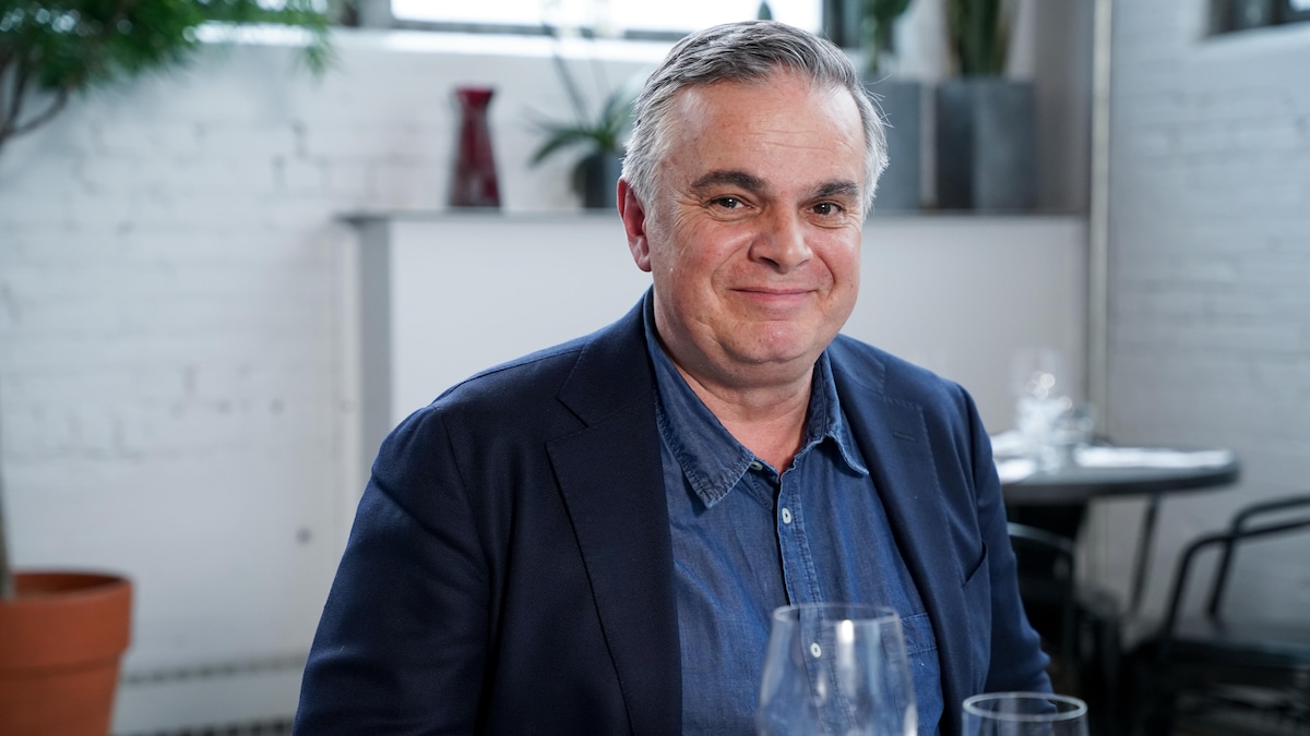 Alexandre Jardin à table, un verre de vin déposé devant lui.
