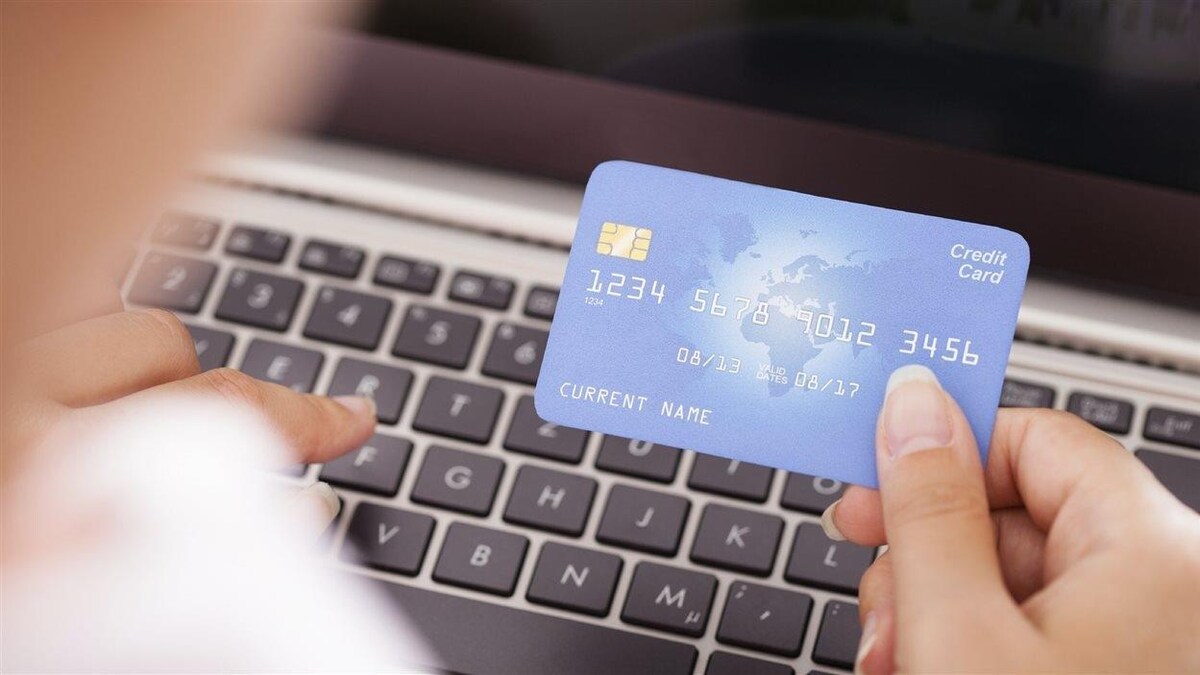 Une femme devant un clavier d'ordinateur tient une carte de crédit dans sa main. 
