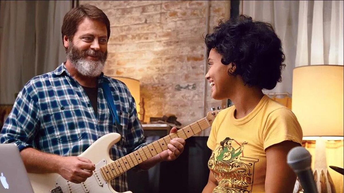 Une jeune fille regarde en souriant un homme barbu qui joue de la guitare.