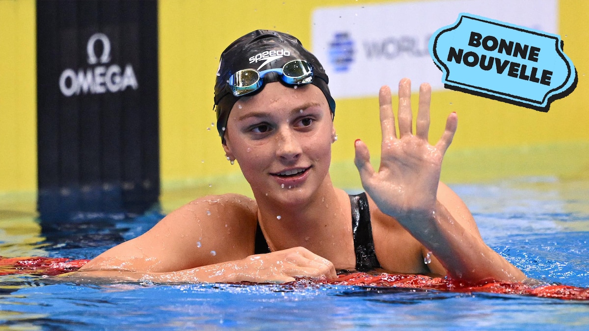 La nageuse canadienne Summer McIntosh, dans la piscine, après sa course, salue quelqu'un, à côté du collant "Bonne nouvelle" de MAJ.
