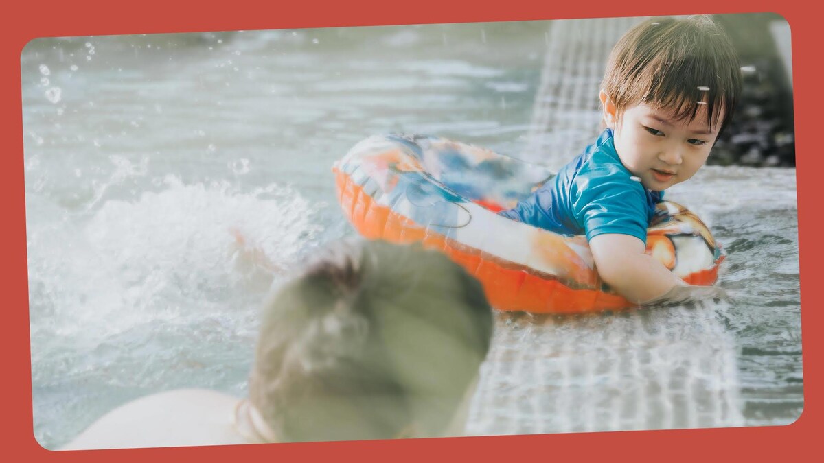 Un petit garçon est dans une bouée à la piscine, il regarde son papa.
