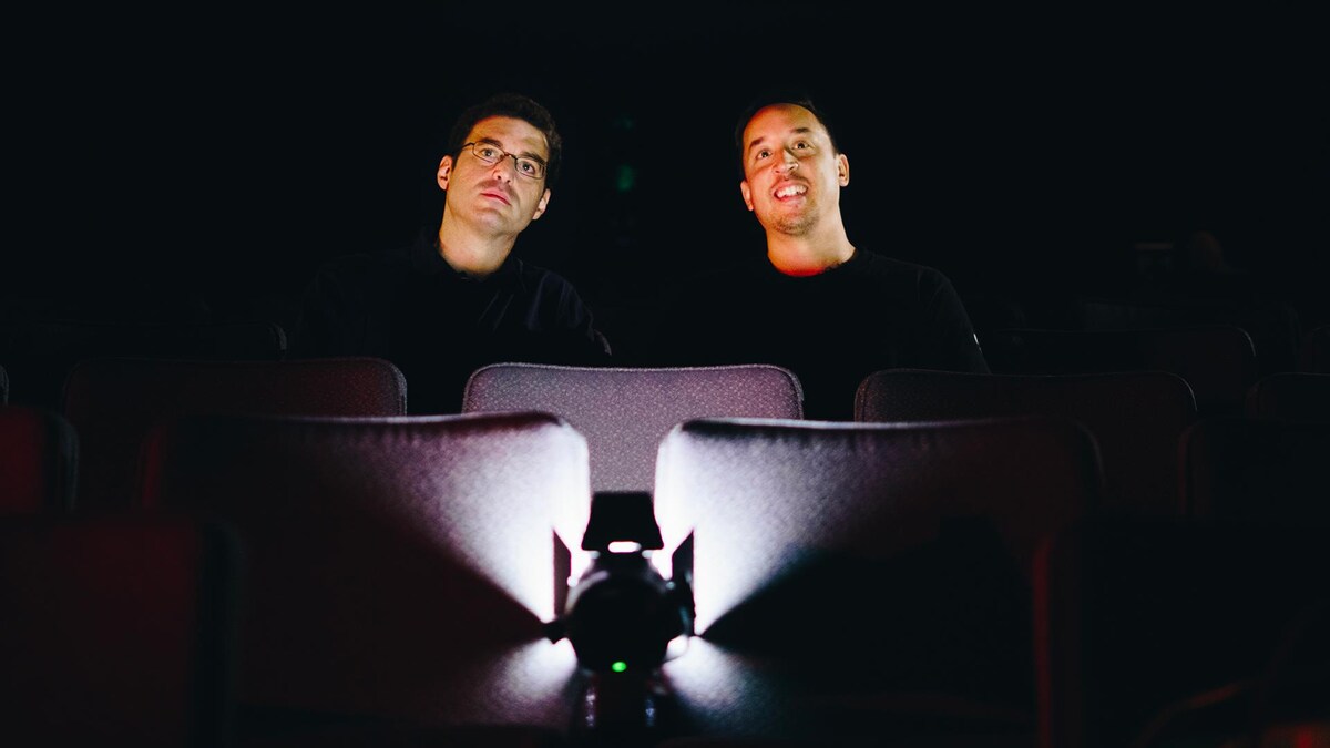 Un journaliste et un professeur de philosophie regardent l'écran dans une salle de cinéma