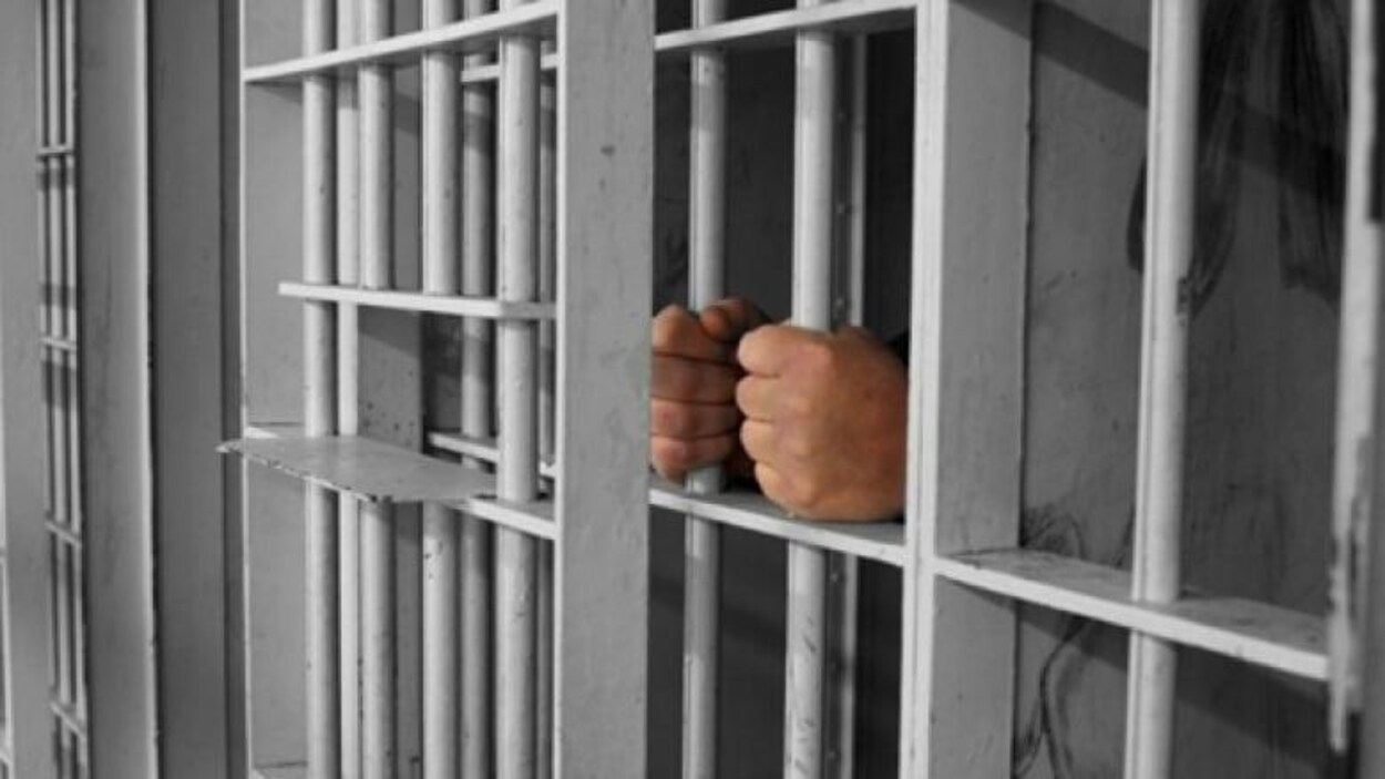 Un homme tient les barreaux d'une cellule de prison.