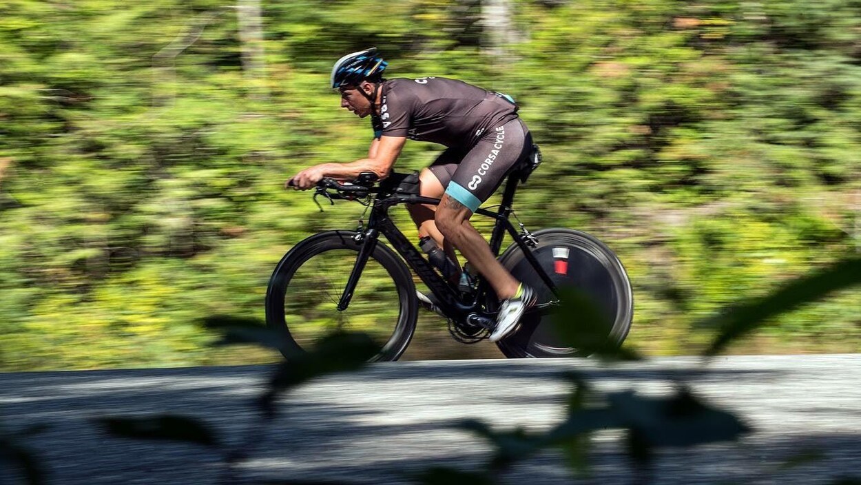 Un homme se promène à vélo sur une route devant un boisé
