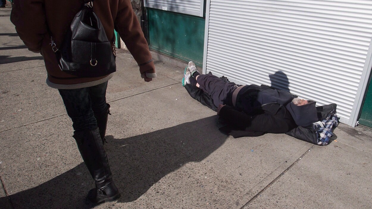 Une femme passe devant un sans-abri étendu sur le trottoir.