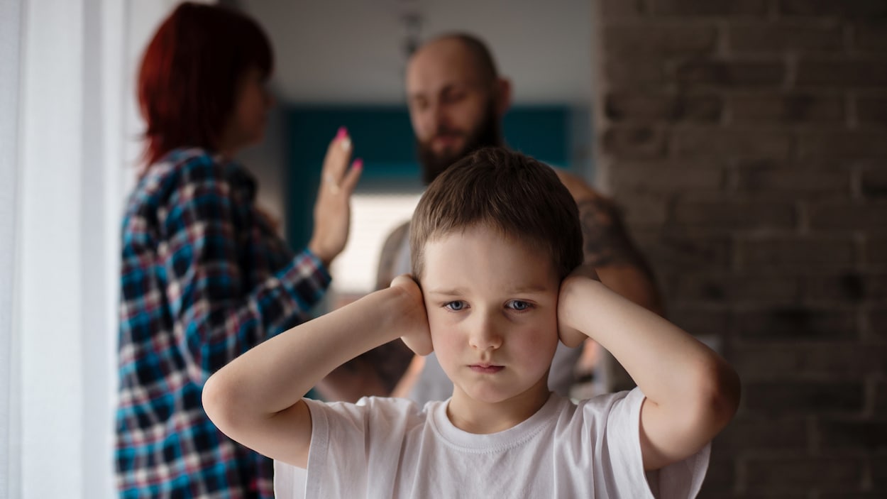 Un enfant se bouche les oreilles pendant que des adultes se disputent derrière lui.