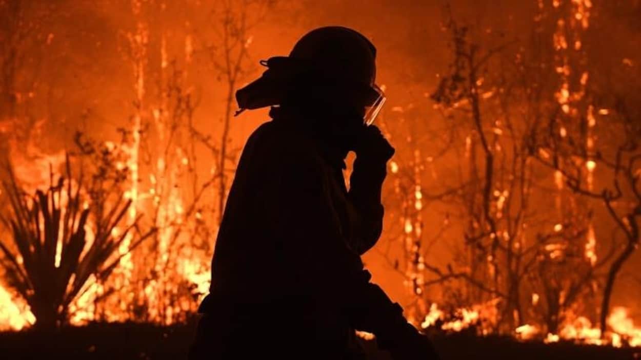 Un pompier marchant avec des flammes derrière lui.