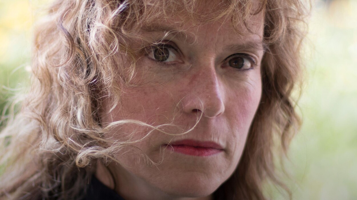 La femme pose à l'extérieur, cheveux bouclés au vent.