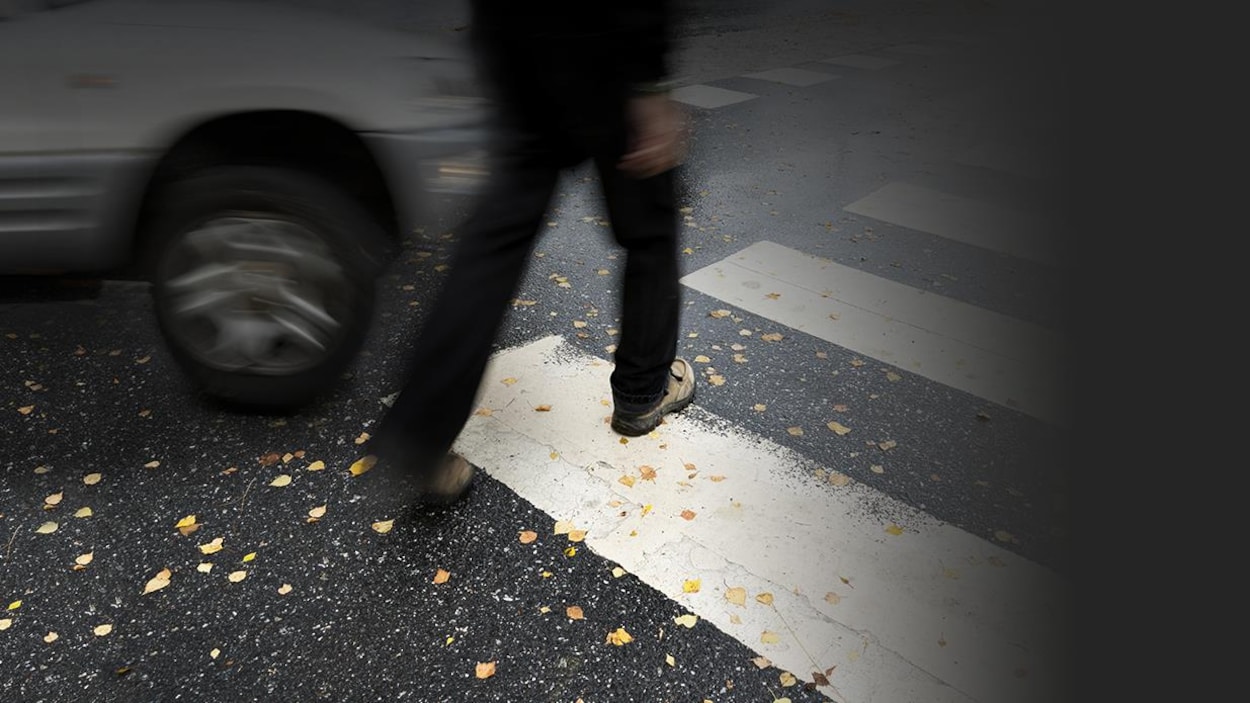 Une voiture frôle un piéton qui traverse une rue
à un passage piétonnier.