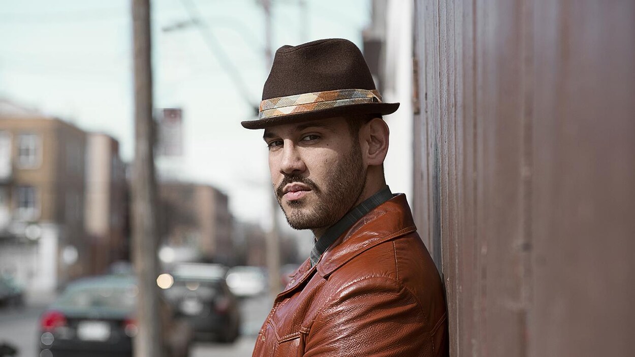 Le chanteur québécois Boogat regarde la caméra sur le côté, adossé à un mur, dans une rue.