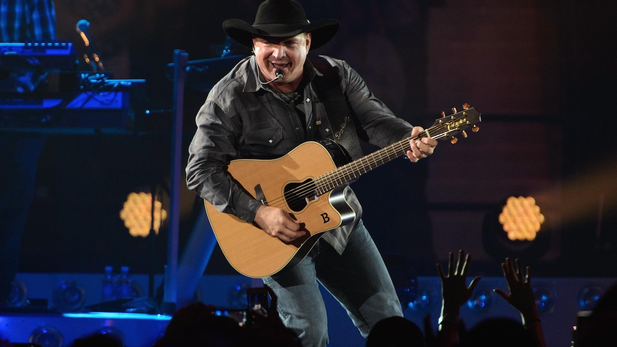 Garth Brooks, sur scène, chante avec une guitare à la main pendant un spectacle.